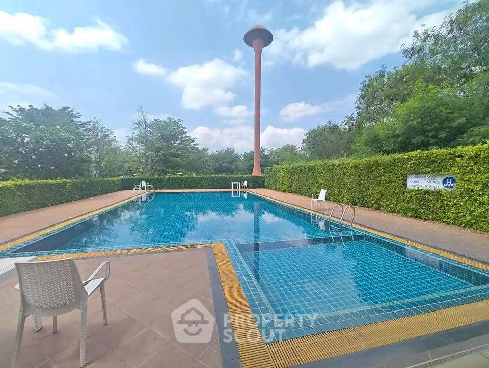 Stunning outdoor pool with lush greenery and clear blue sky, perfect for relaxation and leisure.