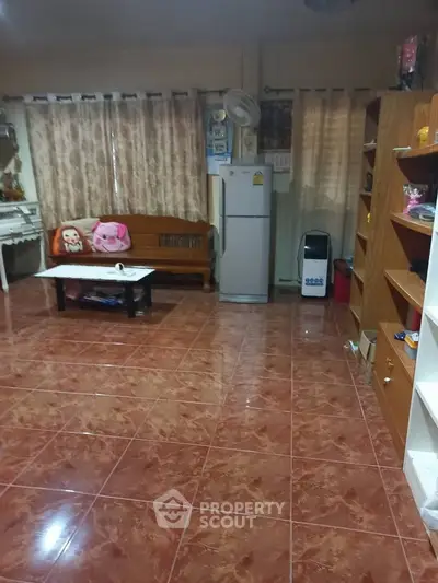 Spacious living room with tiled floor, wooden furniture, and a refrigerator, ideal for cozy gatherings.