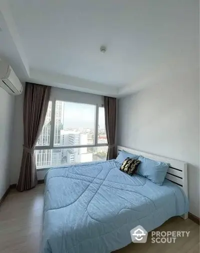 Bright and airy bedroom with large windows offering a city view, complete with a cozy double bed and modern air conditioning unit.