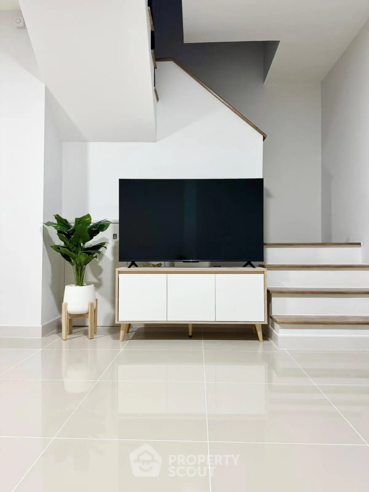 Modern living room with sleek TV stand, large flat-screen TV, and stylish staircase in minimalist design.