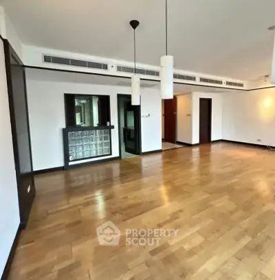 Spacious empty living room with wooden flooring and modern lighting fixtures.
