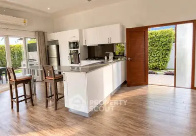 Spacious modern kitchen with open layout and garden view, featuring sleek appliances and wooden flooring.