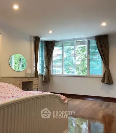 Charming bedroom with large windows and elegant curtains, featuring a cozy bed and stylish vanity.