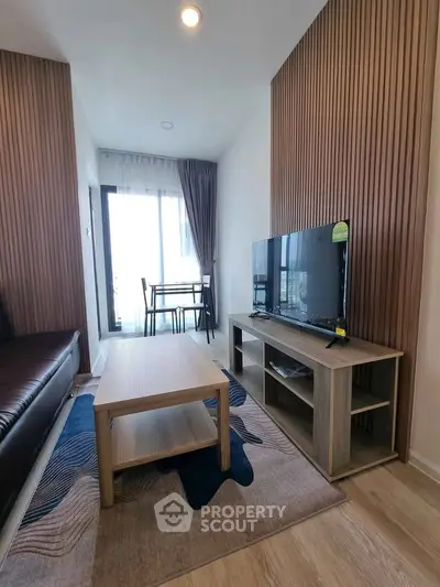 Modern living room with stylish decor and balcony view, featuring a sleek TV setup and cozy seating area.