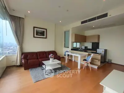 Spacious living room with open kitchen and city view, featuring modern furniture and wooden flooring.