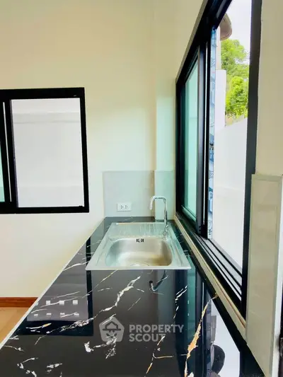 Modern kitchen with sleek black marble countertop and large windows for natural light.