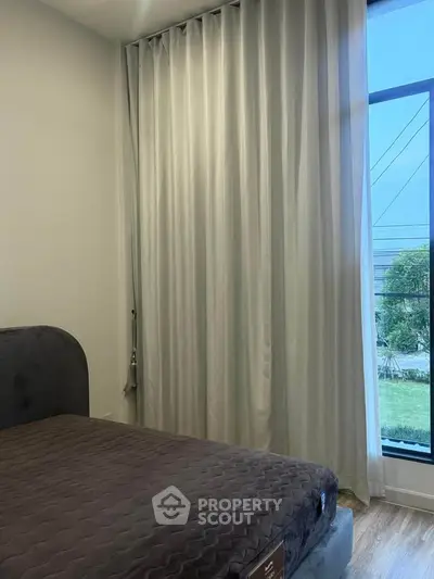 Cozy bedroom with large window and elegant curtains, offering a serene view and natural light.