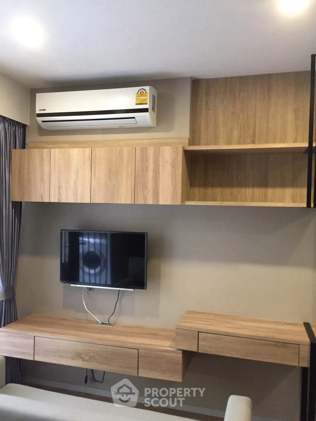 Modern living room with sleek wooden cabinets and mounted TV under air conditioning unit.