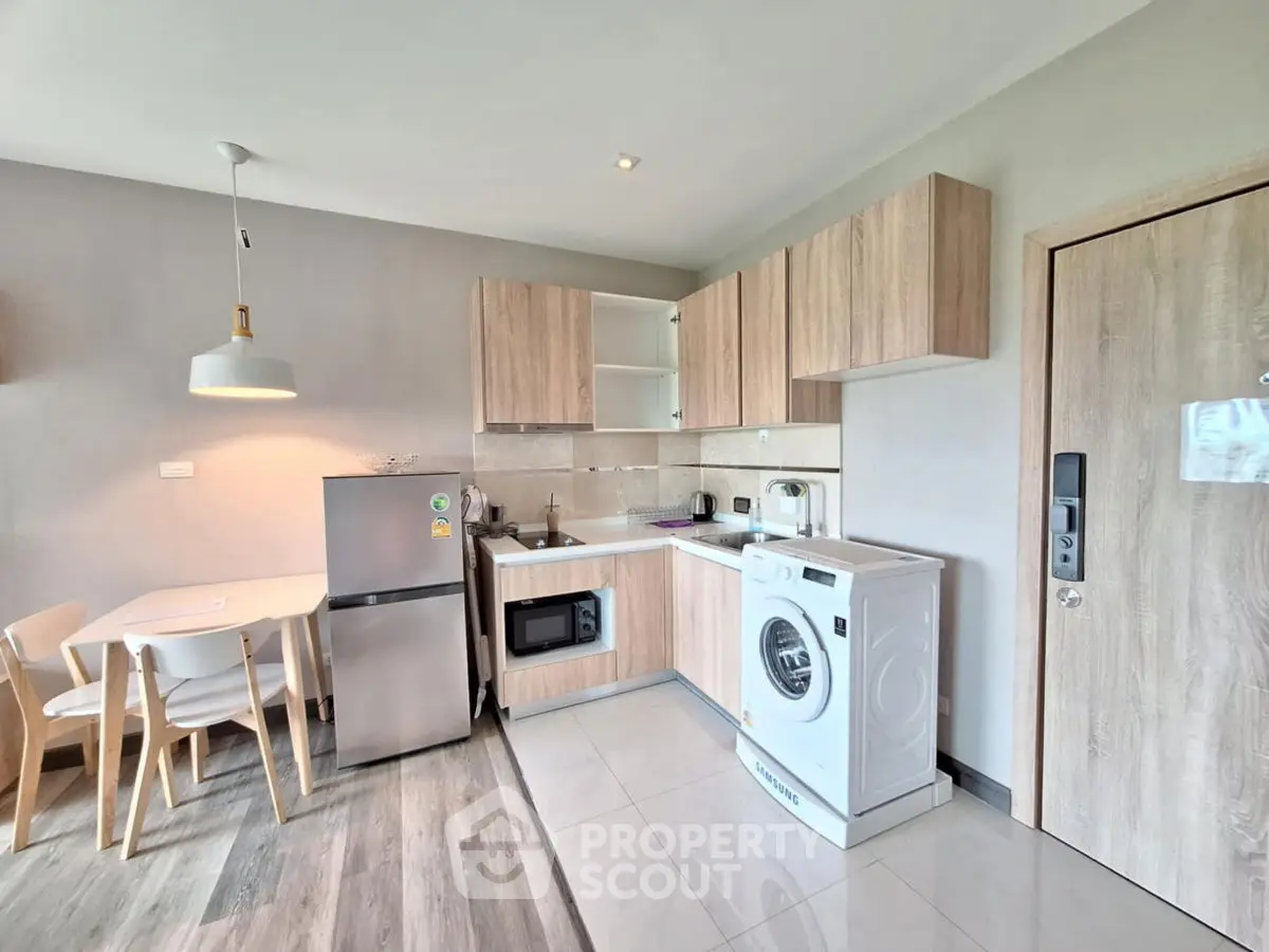 Modern kitchen with washing machine and dining area, featuring sleek wooden cabinets and contemporary lighting.