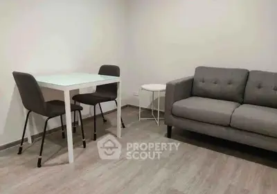 Modern living room with sleek gray sofa and minimalist dining set on wooden flooring.
