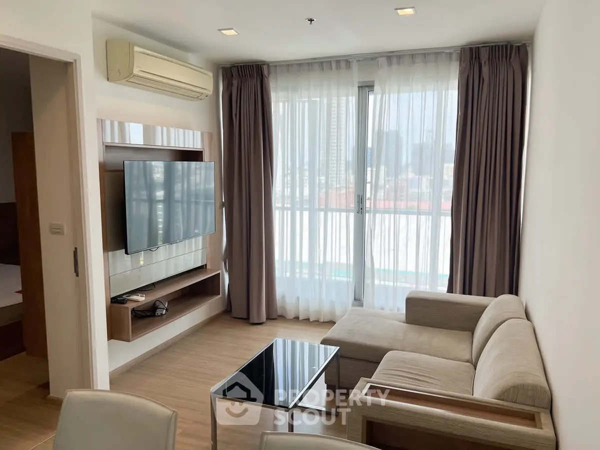 Modern living room with large window and city view, featuring a sleek sofa and wall-mounted TV.