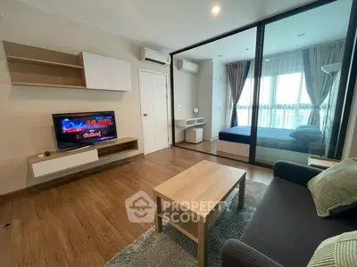Modern living room with wooden flooring and glass partition leading to bedroom, featuring cozy sofa and TV.