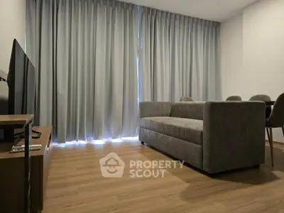Modern living room with sleek grey sofa and dining area, featuring floor-to-ceiling curtains.
