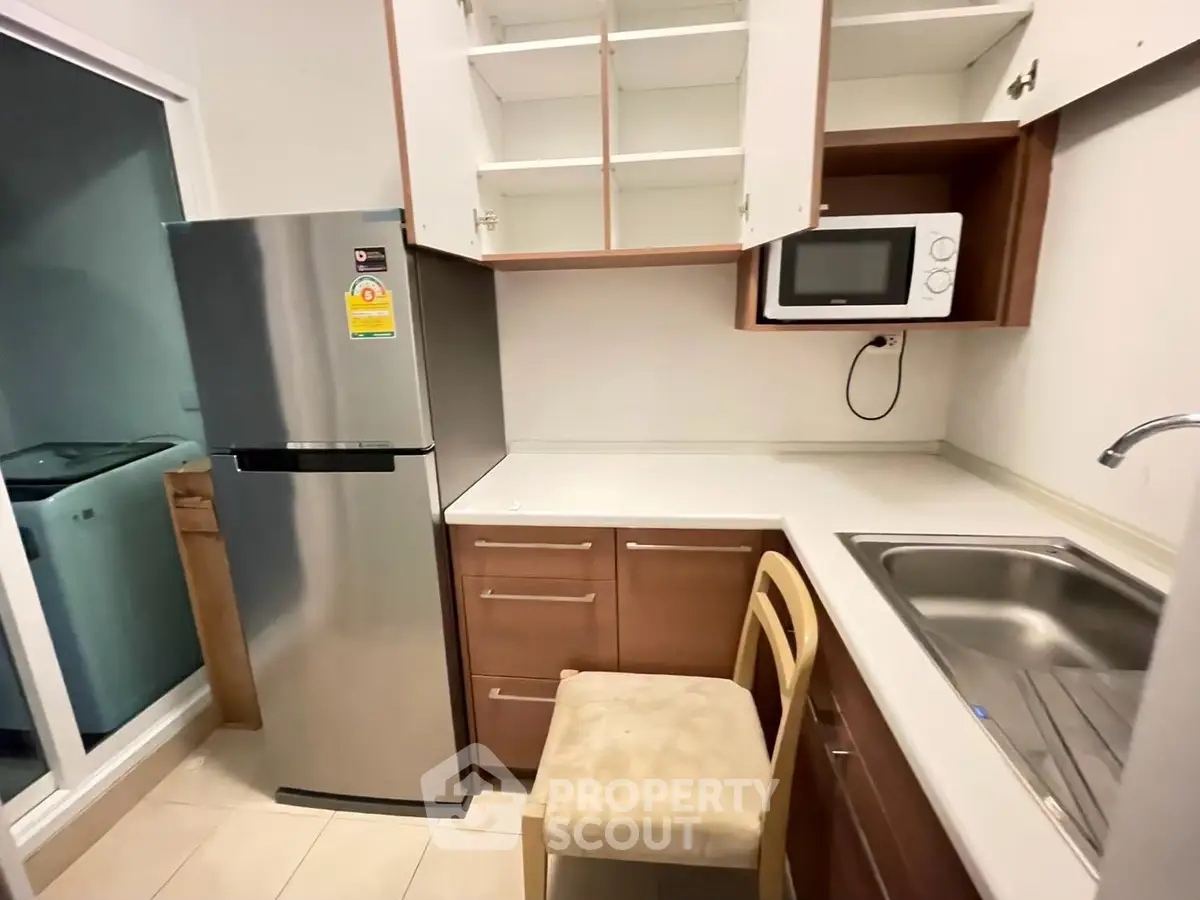 Compact kitchen with stainless steel fridge and microwave, ideal for modern living.