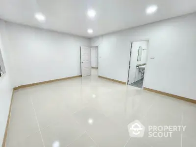 Spacious empty room with glossy tiled flooring and white walls, adjacent to a bathroom.