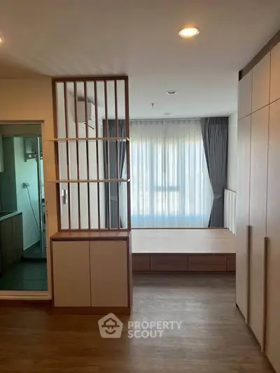 Modern bedroom with wooden flooring and large window, featuring a stylish partition and ample storage space.