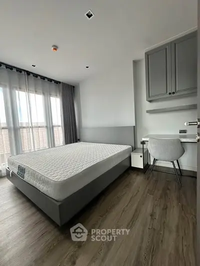 Modern bedroom with large window, stylish furniture, and elegant flooring in a contemporary apartment.