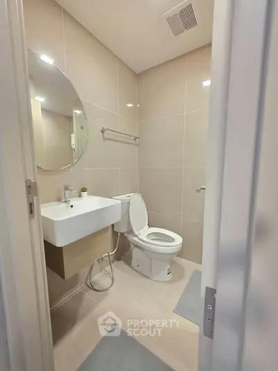 Modern bathroom with sleek fixtures and neutral tones, featuring a round mirror and elegant tile work.