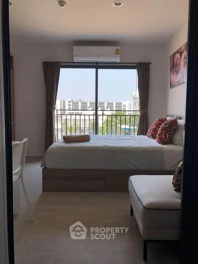 Cozy bedroom with large window and city view, modern decor and comfortable furnishings.