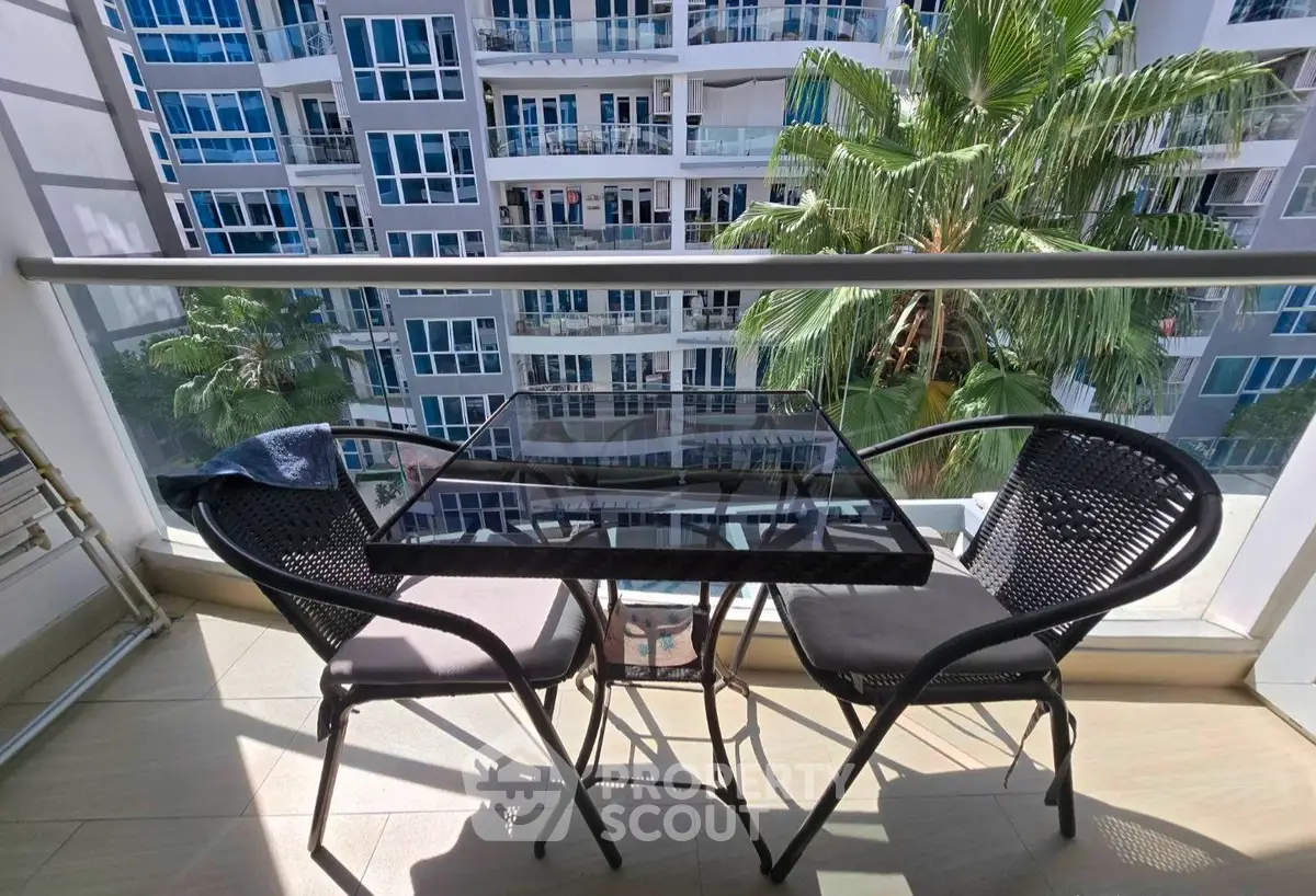 Charming balcony with modern glass table and chairs overlooking lush greenery and contemporary building facade.