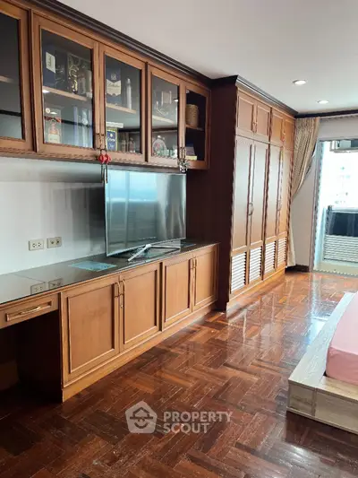 Spacious bedroom with built-in wooden cabinets and large TV, featuring elegant parquet flooring.