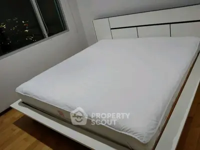 Modern bedroom with sleek white bed and city view window, perfect for urban living.