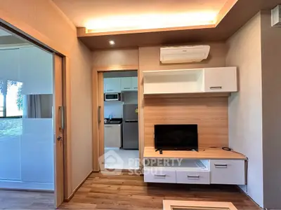 Modern living room with wooden flooring and built-in TV unit, leading to a sleek kitchen area.