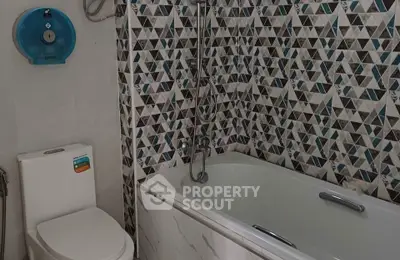 Modern bathroom with geometric tile design and bathtub in stylish apartment.