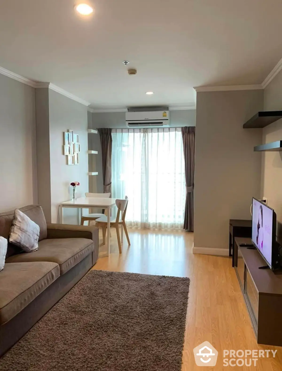 Inviting modern living room with plush seating, sleek TV setup, and a cozy dining area, bathed in natural light from the large window.