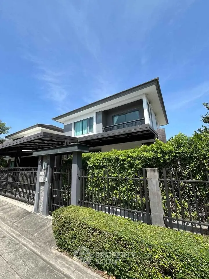 Modern two-story house with lush greenery and sleek fence under clear blue sky.