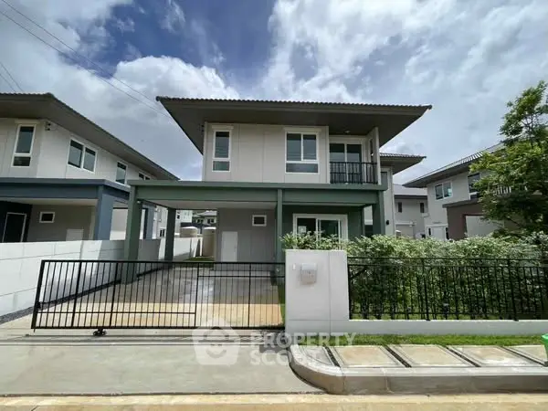 Modern two-story house with gated driveway and lush greenery.
