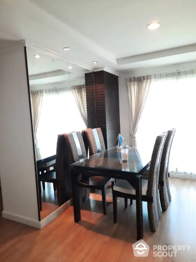 Elegant dining area with modern table and chairs, featuring large mirror and natural light.