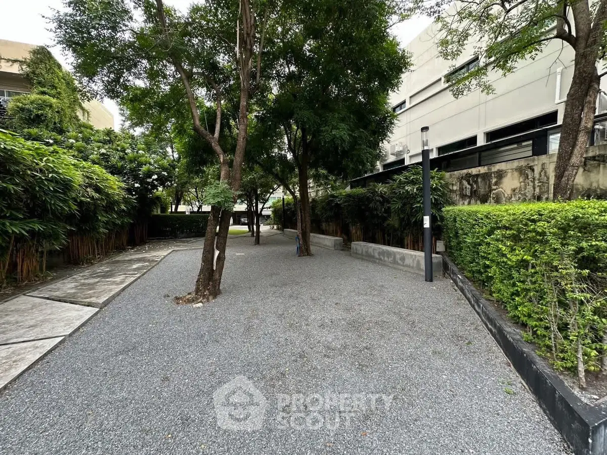Serene garden area with lush greenery and gravel pathway in modern residential complex.