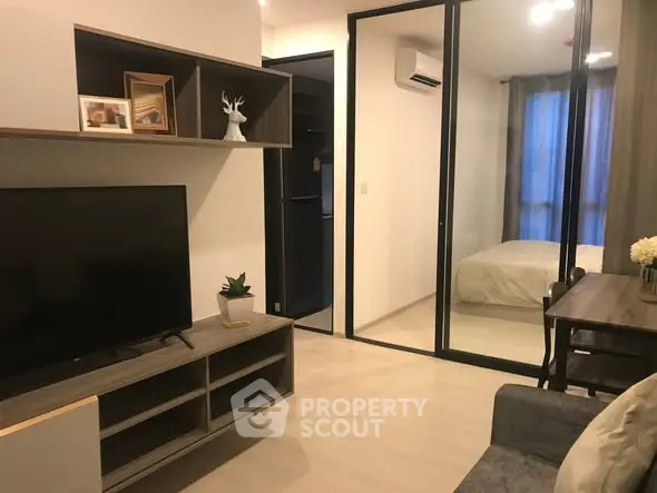 Modern living room with TV, dining area, and view into cozy bedroom through glass doors.