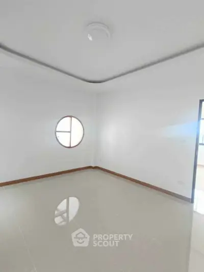 Spacious empty room with unique circular window and glossy tiled floor, perfect for customization.