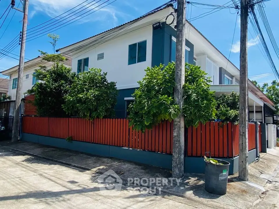 Charming two-story house with vibrant red fence and lush greenery in a serene neighborhood.