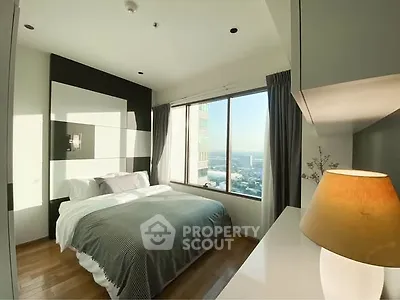 Modern bedroom with large window and city view, featuring cozy bedding and stylish decor.