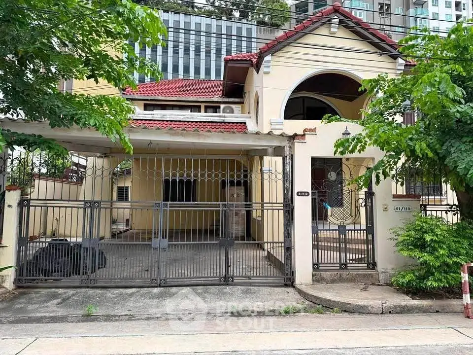 Charming two-story house with gated entrance and lush greenery in urban setting.