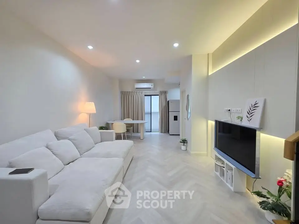 Modern living room with sleek design, featuring a cozy white sofa, wall-mounted TV, and elegant lighting.