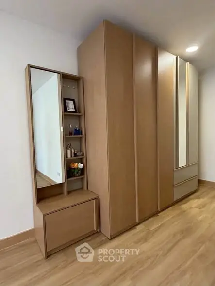 Modern bedroom with sleek wooden wardrobe and vanity mirror, showcasing minimalist design and ample storage space.