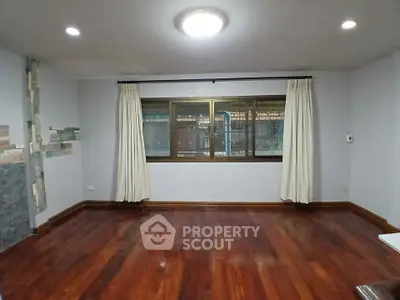 Spacious empty room with wooden flooring and large window, ideal for customization.