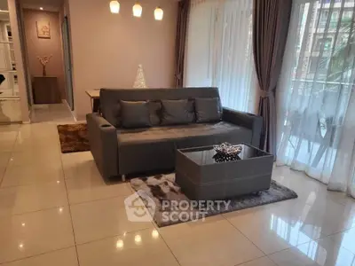 Modern living room with elegant sofa, glass coffee table, and large windows with sheer curtains.
