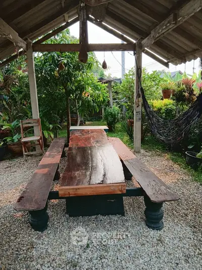 Charming rustic garden with wooden table and hammock under a pergola, perfect for outdoor relaxation.