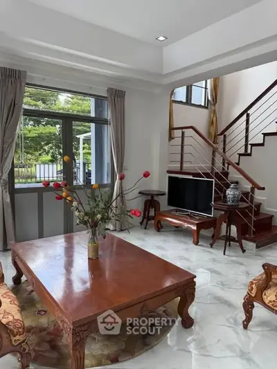 Elegant living room with wooden furniture and staircase, featuring large windows and garden view.