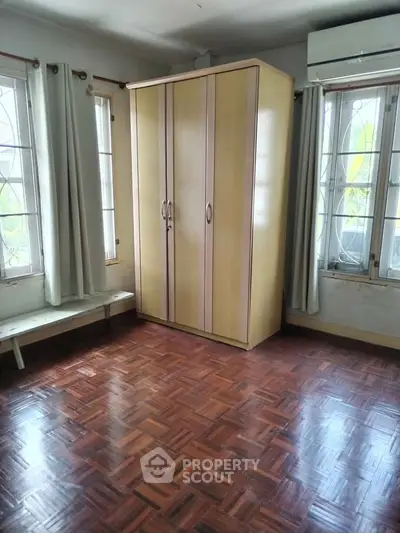 Spacious bedroom with parquet flooring and ample natural light from large windows.
