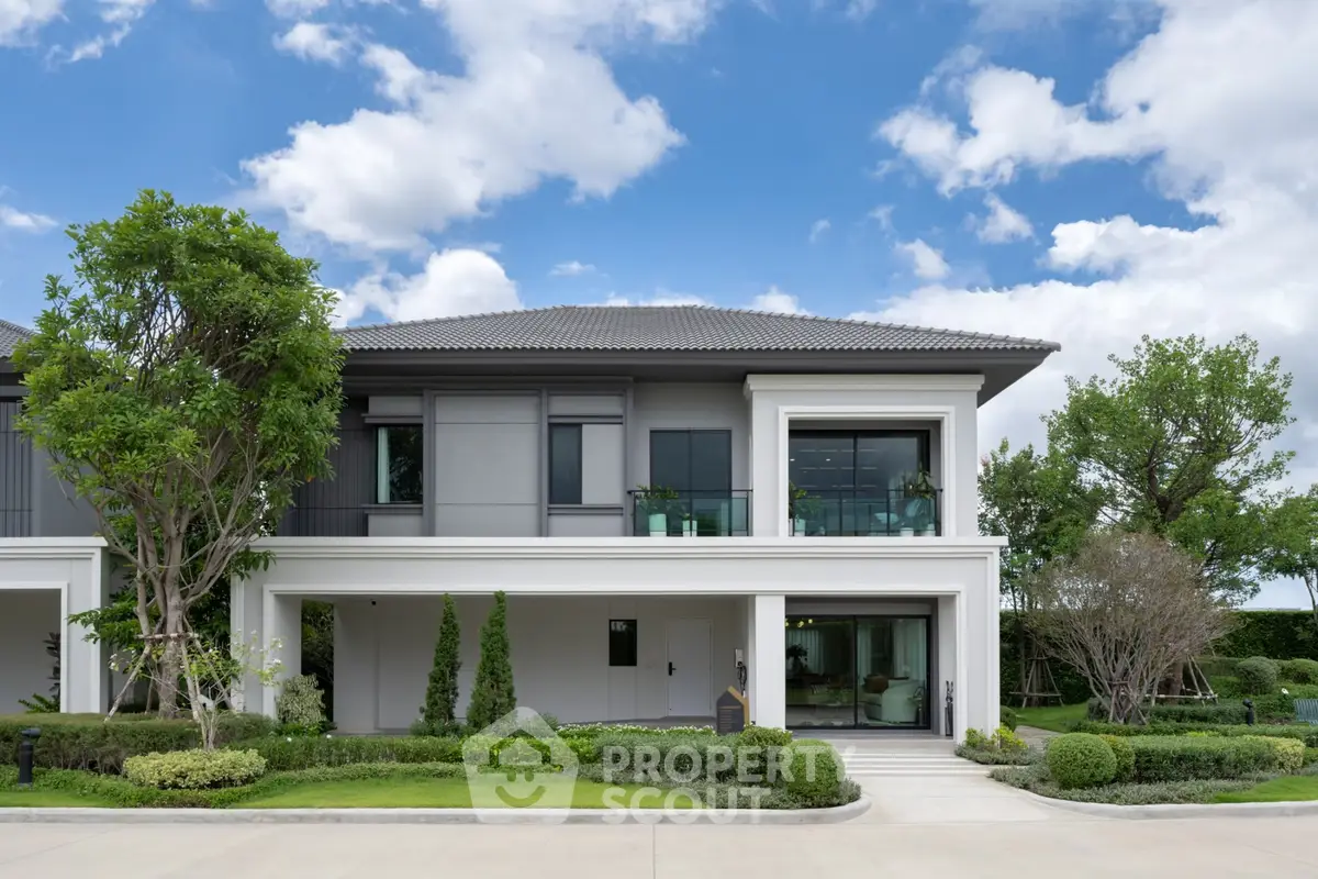 Modern two-story house with lush garden and large windows under a bright blue sky.