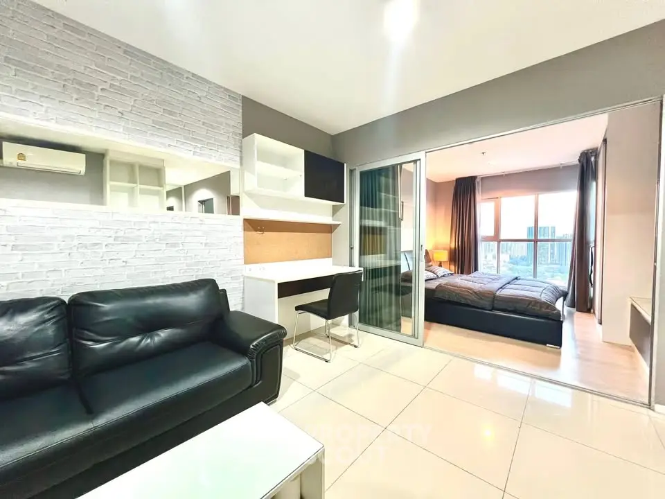 Modern apartment with open living room and bedroom, featuring sleek furniture and large windows.