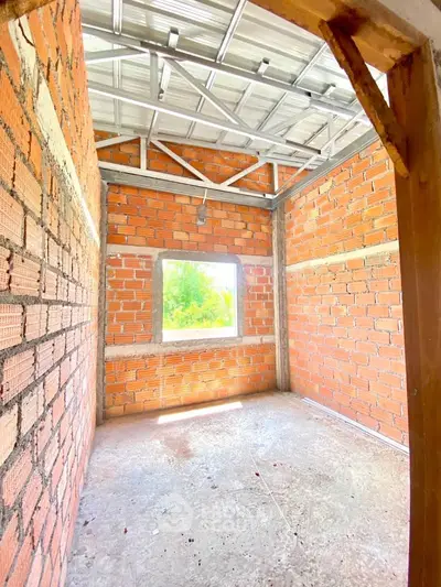 Bright unfinished room with exposed brick walls and metal roof structure, ideal for customization.
