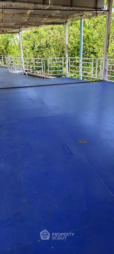 Spacious outdoor balcony with blue flooring and lush greenery view, perfect for relaxation.