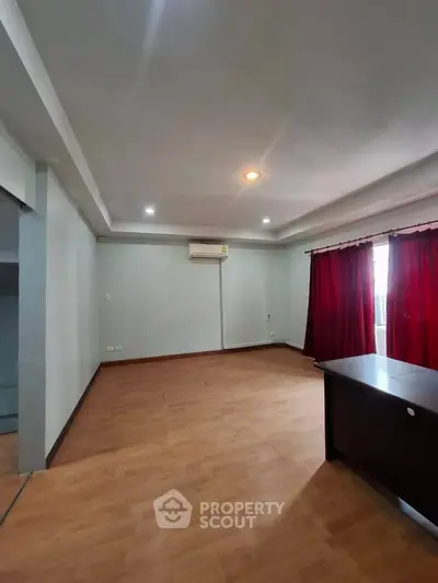 Spacious living room with wooden flooring and red curtains, ideal for modern living.